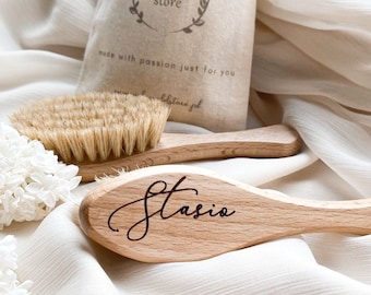 Può includere: Due spazzole per capelli in legno, una con setole naturali e l'altra con un'iscrizione personalizzata che recita "Stasio". Le spazzole sono su uno sfondo di tessuto bianco.