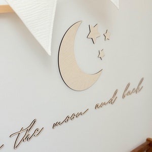 Op de afbeelding: Houten wanddecoratie met een halve maan en sterren met de tekst "to the moon and back".