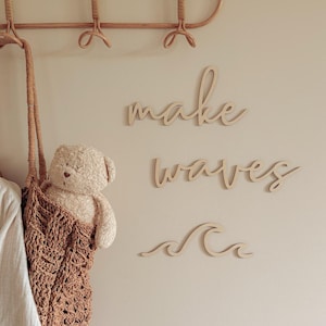 May include: Wooden wall decor with the words "make waves" and a wave design. A teddy bear is partially visible in a brown woven bag hanging on a wall. A wooden coat rack is at the top of the image.