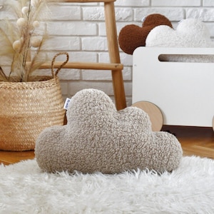 Puede incluir: Una almohada esponjosa en forma de nube de color gris sobre una alfombra de piel sintética blanca. La almohada tiene una pequeña etiqueta que dice "Knitted".