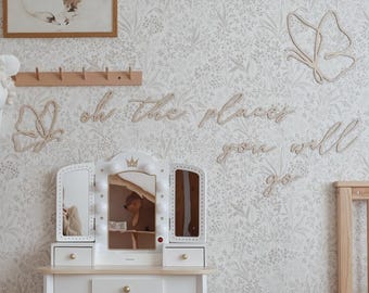 Può includere: Un set di vanità per bambini bianco e beige con sgabello abbinato. La vanità ha uno specchio a tre ante con luci e un cassetto. La parete dietro la vanità ha un motivo floreale, decorazioni a farfalla in legno e il testo "Oh the places you will go."