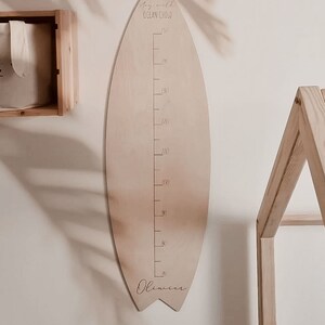 May include: A wooden surfboard-shaped growth chart with a ruler marked in centimeters, a wave graphic, and the text "stay wild ocean child". The chart is personalized with the name "Oliver" at the bottom.