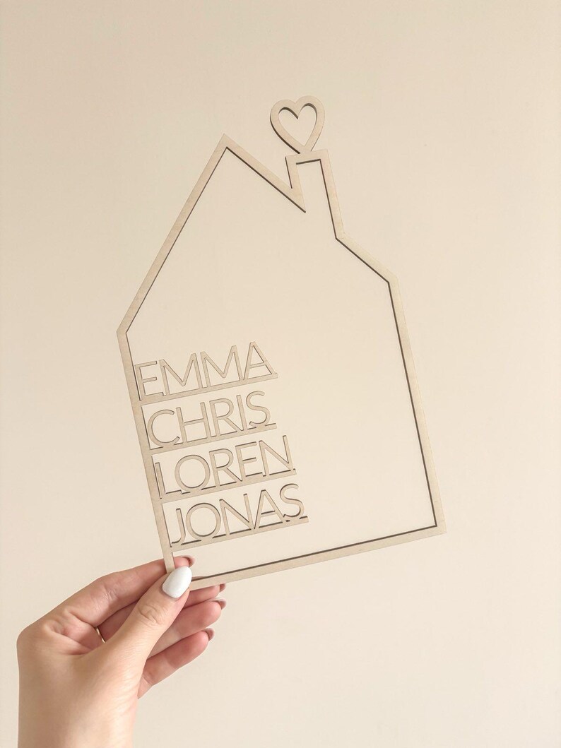 May include: A wooden house-shaped sign with the names "Emma", "Chris", "Loren", and "Jonas" inscribed on it. The house has a heart-shaped chimney.