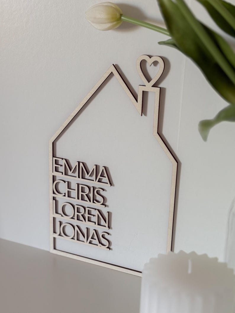 May include: Wooden house-shaped wall decor with a heart on top and the names Emma, Chris, Loren, and Jonas written in a modern font.