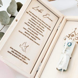 May include: A wooden box with a dove and church design engraved on the lid. The box is open and contains a white envelope with a rolled up bill of money inside. The box also has a message inside that reads "Liebe Emma Zur heiligen Taufe w&uuml;nschen wir dir von Herzen Gottes reichen Segen, unendlich viel Liebe. Gesundheit und Freude auf deinem Lebensweg. M&ouml;gest du stets von Gottes gute begleitet und von deinen Liebsten beh&uuml;tet werden. Alles Gute f&uuml;r deine Zukunft! Zum Andenken an den Tag der heiligen Taufe - Patin Elisabeth mit Familie"