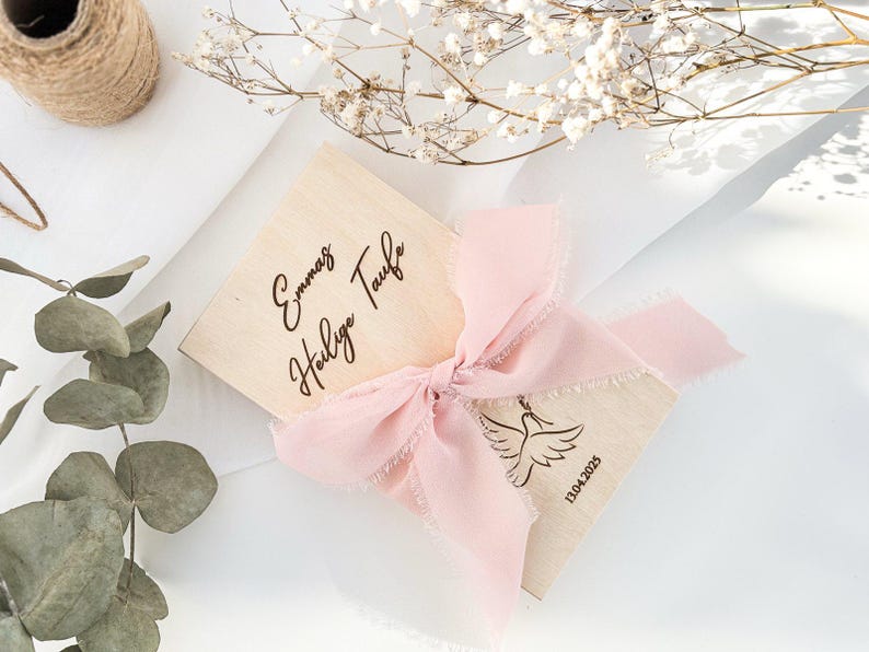 K&ouml;nnte beinhalten: Eine Holzkiste mit einem rosa Band darum gebunden. Die Kiste ist mit dem Text "Emma's Holy Baptism" und dem Datum "13.04.2023" graviert.