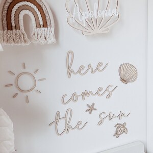 May include: Wooden wall decor with a sun, a starfish, a turtle, a seashell, and the words "here comes the sun". The name "Apolonia" is written on a seashell.