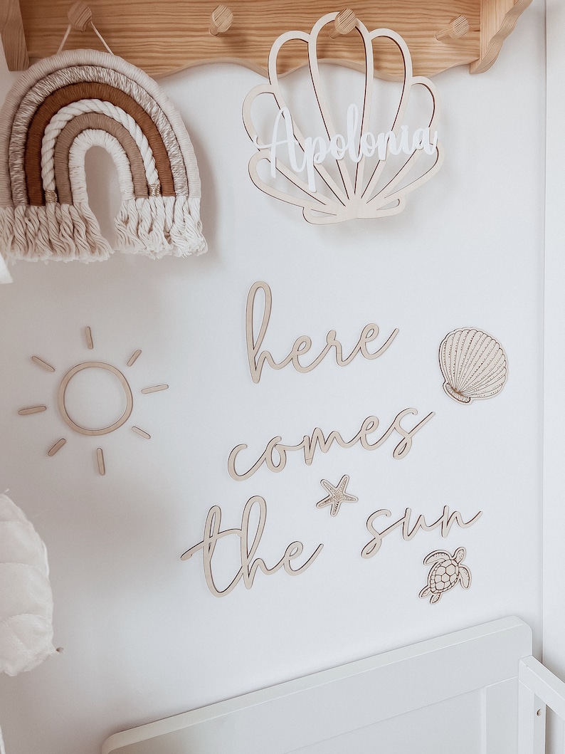 May include: Wooden wall decor with a sun, a starfish, a turtle, a seashell, and the words "here comes the sun". The name "Apolonia" is written on a seashell.