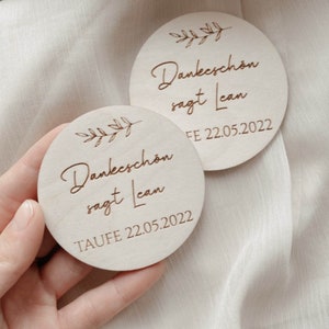 Könnte beinhalten: Zwei runde Holzschilder mit einem Blattwerk-Design und dem Text "Danke schön sagt Lean" mit den Daten "TAUFE 22.05.2022" und "FE 22.05.2022".