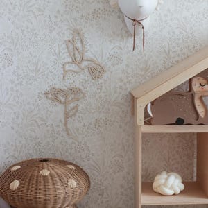 Peut inclure: Un abat-jour en osier brun clair en forme de champignon repose sur une surface blanche avec un papier peint à motifs floraux. Une étagère en bois avec une figurine de cerf en bois brun et une boule de corde nouée blanche se trouve à droite de l'image. Deux découpes d'oiseaux-mouches en bois sont fixées au mur.