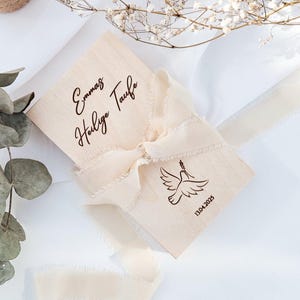 May include: A wooden box with a white ribbon tied around it. The box is engraved with the text "Emma's Holy Taufe" and the date "13.04.2023".