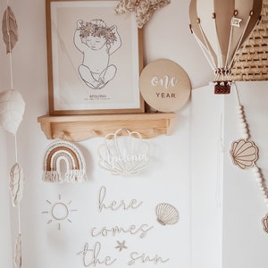 May include: A nursery room decorated with a white and brown hot air balloon, a wooden sign that says "one year", a wooden rainbow, a wooden sun, and a wooden sign that says "here comes the sun".