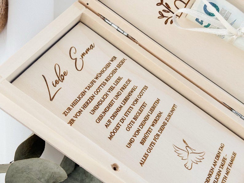 May include: A wooden box with a dove design and the text "Liebe Emma" engraved on the lid. The text inside the box reads "Zur heiligen Taufe w&uuml;nschen wir dir von Herzen Gottes reichen Segen, unendlich viel Liebe, Gesundheit und Freude auf deinem Lebensweg. M&ouml;gest du stets von Gottes G&uuml;te begleitet und von deinen Liebsten beh&uuml;tet werden. Alles Gute f&uuml;r deine Zukunft."