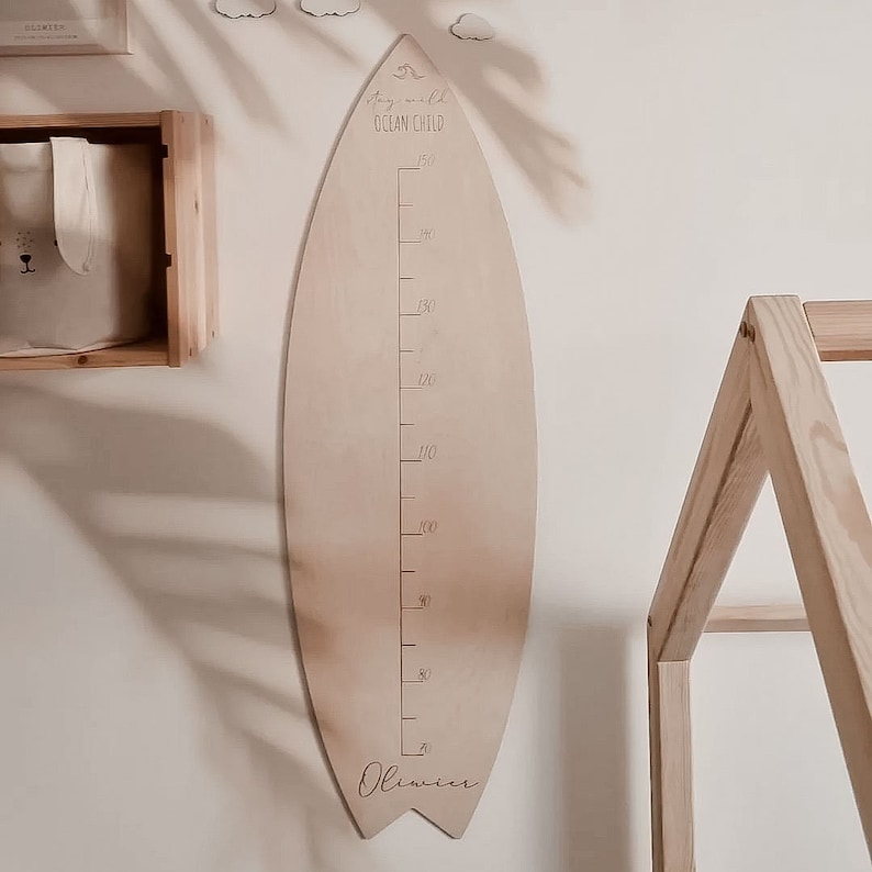 May include: A wooden surfboard-shaped growth chart with a ruler marked in centimeters, a wave graphic, and the text "stay wild ocean child". The chart is personalized with the name "Oliver" at the bottom.