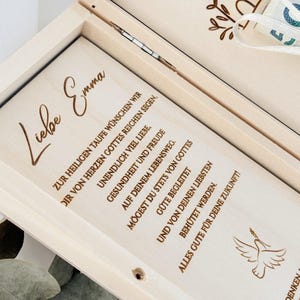 K&ouml;nnte beinhalten: Eine Holzkiste mit einem Taubenmotiv und dem Text "Liebe Emma" auf dem Deckel. Der Text setzt sich im Inneren der Kiste mit einer Botschaft fort, die dem Empf&auml;nger alles Gute zur Taufe w&uuml;nscht.