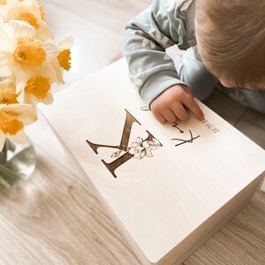 Peut inclure: Une bo&icirc;te &agrave; souvenirs en bois avec une lettre "K" grav&eacute;e personnalis&eacute;e et un motif floral. La bo&icirc;te est de couleur brun clair et a un fond blanc. Le texte "Jacob" est grav&eacute; sur la bo&icirc;te.