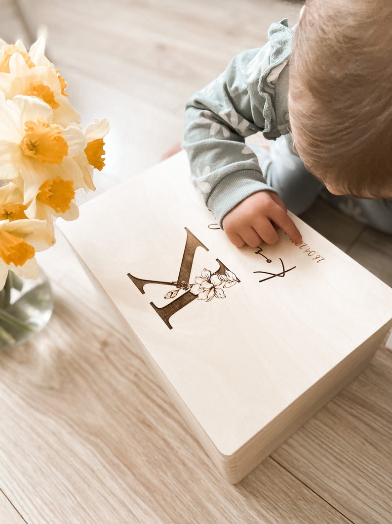 Peut inclure: Une bo&icirc;te &agrave; souvenirs en bois avec une lettre "K" grav&eacute;e personnalis&eacute;e et un motif floral. La bo&icirc;te est de couleur brun clair et a un fond blanc. Le texte "Jacob" est grav&eacute; sur la bo&icirc;te.