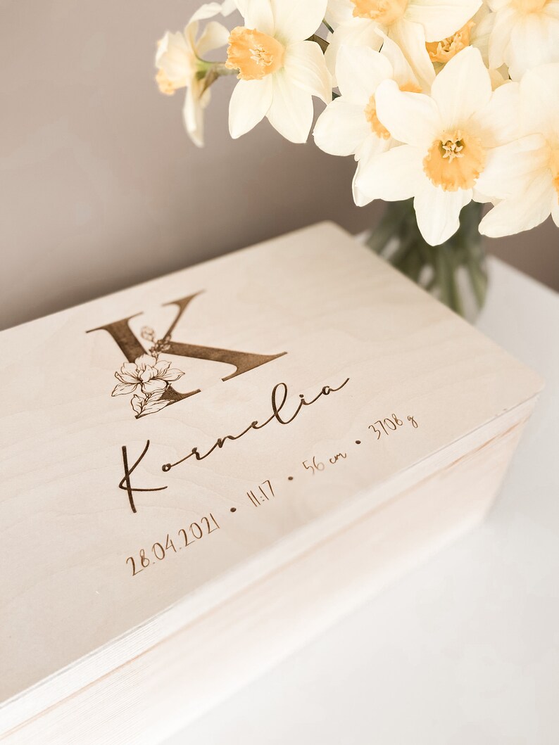 Peut inclure: Une bo&icirc;te &agrave; souvenirs en bois clair avec une inscription personnalis&eacute;e. L'inscription indique "K" avec un motif floral, "Kornelia", "28.04.2021", "11:17", "56 cm" et "3708 g".