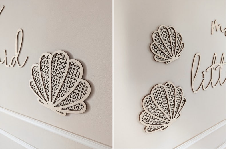 May include: Wooden wall art featuring a seashell design with a woven pattern. The image shows multiple seashell cutouts and cursive text on a neutral-colored wall. The overall theme is coastal decor.