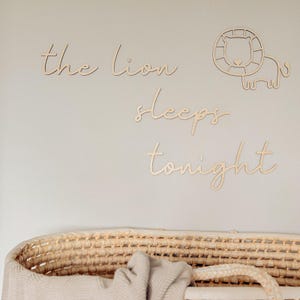 May include: Wooden wall decor with the phrase "the lion sleeps tonight" in a cursive font. The decor includes a cutout of a lion's head and body.