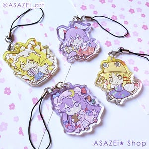 May include: Four clear acrylic charms with cartoon character designs. Each charm has a different character in various colors, including yellow, purple, and blue. Each charm has a black lanyard attached. The shop name "ASAZEl Shop" is printed at the bottom.