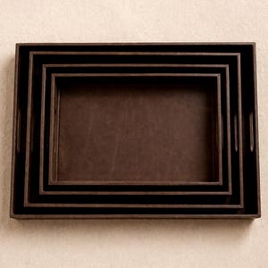 Peut inclure: Ensemble de quatre plateaux de service rectangulaires bruns emboîtables. Les plateaux ont un extérieur brun foncé et un intérieur brun clair. Chaque plateau est de taille légèrement différente, conçu pour s'emboîter pour le rangement.