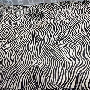 May include: A large piece of fabric with a striking zebra stripe pattern. The black and white design features flowing, curved stripes, creating a dynamic visual texture. The fabric appears to be draped, showcasing its flexibility and potential uses.