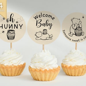 May include: Set of 24 Winnie the Pooh themed cupcake toppers. The toppers feature a honey pot, bees, and the text "oh hunny", "Welcome Baby", and "someone sweet is coming".