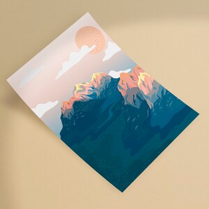 May include: A print featuring a mountain range under a peach-colored sun and clouds. The mountain peaks are illuminated with orange and yellow hues, contrasting with the dark blue of the mountain's base. The artwork is on a white rectangular paper.