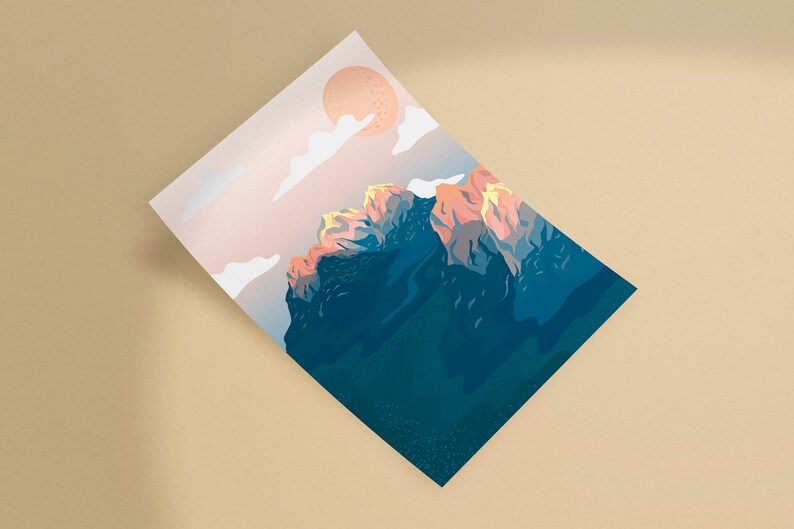May include: A print featuring a mountain range under a peach-colored sun and clouds. The mountain peaks are illuminated with orange and yellow hues, contrasting with the dark blue of the mountain's base. The artwork is on a white rectangular paper.