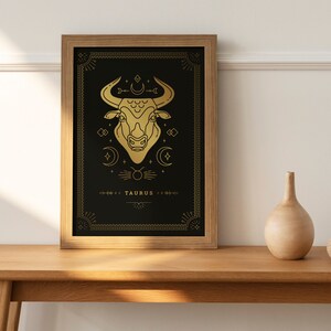 May include: Gold framed print with a black background and a gold outline of a bull's head with a crescent moon and stars. The text "TAURUS" is at the bottom of the print.