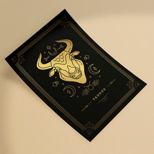 May include: A black and gold print with a stylized illustration of a bull's head and the word "TAURUS" in a decorative font.