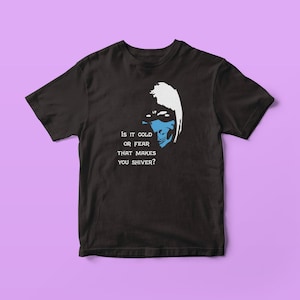 以下が含まれることがあります： マスクをした人物の白と青のグラフィックが描かれた黒いTシャツ。シャツのテキストは「Is it cold or fear that makes you shiver?」です