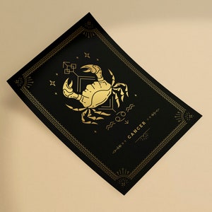 May include: A black and gold zodiac print featuring the Cancer constellation with a crab illustration and the word "CANCER" in a decorative font.