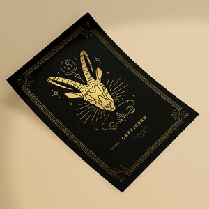May include: Black rectangular card with a gold Capricorn zodiac illustration. The design features a goat head, celestial symbols, and the word "CAPRICORN" in gold. The card has a decorative border.