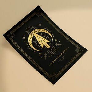 May include: A black and gold poster with a stylized illustration of the Sagittarius zodiac sign. The sign is depicted as an arrow with a crescent moon and stars. The text "SAGITTARIUS" is written in gold lettering.