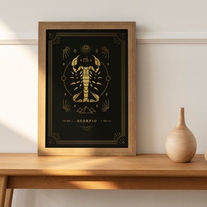 May include: A framed art print featuring a gold scorpion zodiac symbol on a black background. The artwork includes decorative elements and the word "SCORPIO" at the bottom. A wooden vase and sphere sit on a wooden table.