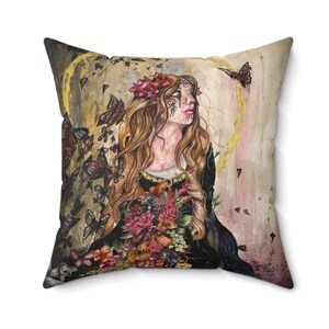 May include: A throw pillow with a watercolor painting of a woman with long red hair wearing a floral crown and a black dress. She is surrounded by butterflies and flowers. The background is a yellow and pink ombre.