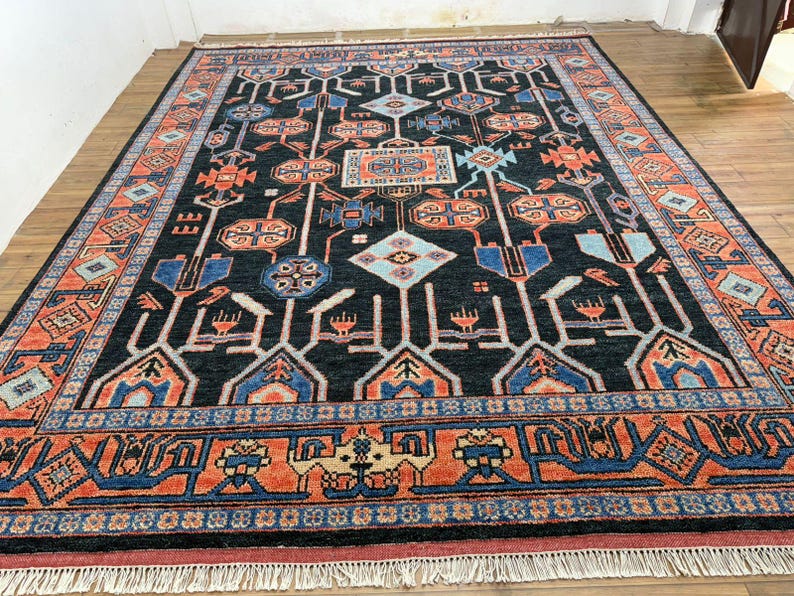 May include: A large, rectangular rug with a dark background and intricate geometric patterns in shades of orange, blue, and white. The rug has a detailed border and fringe along the edges, suitable for home decor.