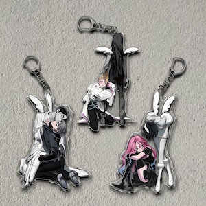 May include: Four acrylic keychains featuring anime-style illustrations of characters in various poses. The keychains have silver-colored metal clasps. The characters are depicted in black, white, and pink, with some wearing angel wings.