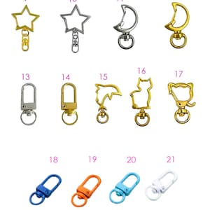 May include: A selection of metal keychain accessories, including split rings, lobster clasps, and swivel clasps. Some clasps are shaped like stars, hearts, and moons. Various colours are available, including blue, orange, and pink.