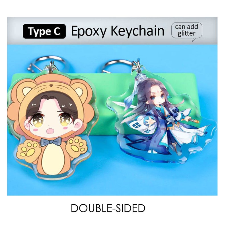 May include: Two double-sided epoxy keychains. One features a cartoon character in a bear costume, the other a character in blue robes. The keychains have silver key rings and the text "Type C Epoxy Keychain" and "can add glitter". The word "DOUBLE-SIDED" is also visible.