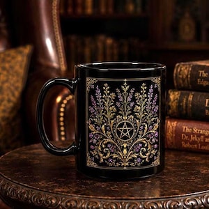 Może przedstawiać: Czarny ceramiczny kubek z botaniczną ilustracją w kolorze złotym i fioletowym, wyśrodkowaną wokół symbolu pentagramu. Wzór zawiera skomplikowane filigranowe detale oraz motywy kwiatowe ujęte w prostokątną ramkę na przedniej stronie.