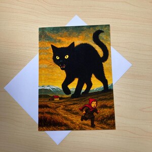 May include: Greeting card featuring a black cat with glowing yellow eyes, looming over a child in a red hooded cloak running across a field. The background shows a sunset over mountains and a small house. The card is on a white envelope.