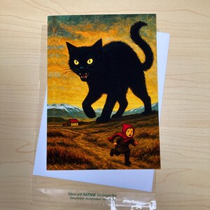 May include: Greeting card featuring a black cat with yellow eyes, chasing a child in a red hooded cloak across a field. The background shows a sunset and a small house. The card is in a clear plastic sleeve.