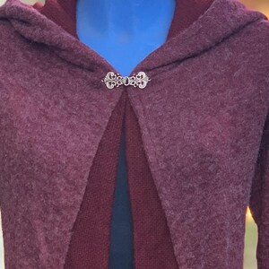 Op de afbeelding: Een bordeauxrode hooded cardigan met een zilveren sluiting. De cardigan is gemaakt van een zacht, pluche materiaal.