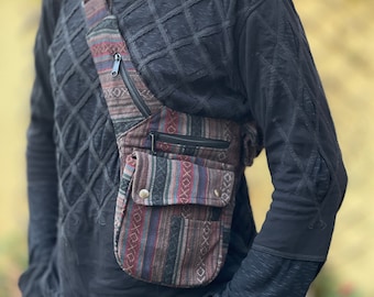 May include: A brown and black patterned crossbody bag with a zippered pocket and a flap closure. The bag is worn over a black shirt with a textured design.