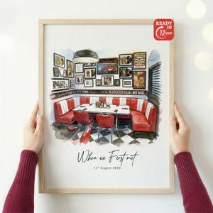 Puede incluir: Impresión en acuarela enmarcada de un interior de restaurante con asientos rojos y suelo ajedrezado en blanco y negro. La impresión incluye el texto "When we First met" y la fecha "11 de agosto de 2022". Marco de madera clara.