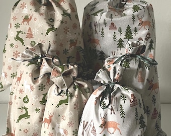 May include: Five fabric gift bags with drawstring closures. The bags feature a festive winter pattern with deer, trees, and snowflakes in shades of beige, green, and brown. The bags are tied with dark green ribbons.