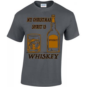May include: A dark gray t-shirt with the text "My Christmas Spirit is Whiskey" in orange and black. The design includes a glass of whiskey with ice and a bottle of whiskey labeled "Whiskey".